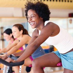 Women sitting on exercising bikes in gym, side view