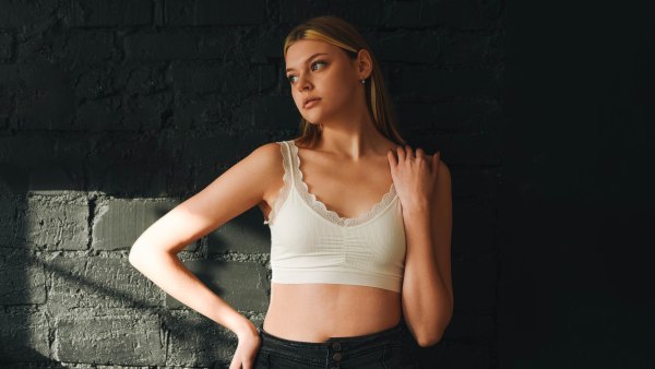 Portrait of a beautiful girl in a white top against a dark wall. Beautiful girl. Blonde. White top. Natural makeup.