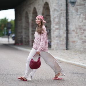 COPENHAGEN, DENMARK - JULY 06: Evi Wave wears a red and white check headscarf, long straight brown hair with a center part, a pink and white knit crew-neck sweater with long sleeves, cream white satin wide-leg pants, a burgundy woven shoulder bag, burgundy sandals shoes, outside Marimekko, during Copenhagen Fashion Week Spring/Summer 2027, on July 06, 2026 in Copenhagen, Denmark (Photo by Edward Berthelot/Getty Images)