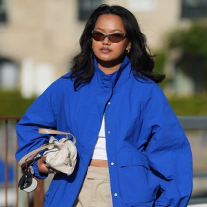 COPENHAGEN, DENMARK - JULY 06: A guest wears long wavy black hair with a center part, brown rectangular sunglasses with tinted lenses, a cobalt blue zip-front jacket with a high collar, a white crop top, beige wide-leg knee-length shorts, a Chanel beige crossbody bag, white leather lace-up ballet flat shoes, outside Collina Strada, during Copenhagen Fashion Week Spring/Summer 2027, on July 06, 2026 in Copenhagen, Denmark (Photo by Edward Berthelot/Getty Images)