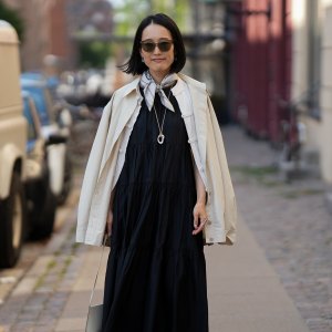 COPENHAGEN, DENMARK - AUGUST 3: A guest is seen wearing a black tiered midi dress layered with an off-white jacket draped over the shoulders, a printed silk neck scarf, cream shoulder bag, black leather fisherman sandals with cream socks, and tinted sunglasses outside the Frama Breakfast during Copenhagen Fashion Week Spring/Summer 2027 on August 3, 2026 in Copenhagen, Denmark. (Photo by Moritz Scholz/Getty Images)