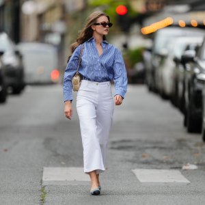 Segolene Hyppolite wears sunglasses, a blue and white oversized shirt from Tommy Hilfiger, a raffia beige bag from Vanessa Bruno, high waist white denim pants from Vanessa Bruno, Chanel slingback shoes in blue denim with black tips, during a street style fashion photo session, on May 20, 2024 in Paris, France.