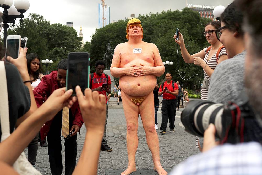 Bystanders photograph and pose with a statue of a naked GOP presidential candidate Donald Trump that appeared in Union Square Park before it was hauled away this morning on August 18, 2016 in New York City.