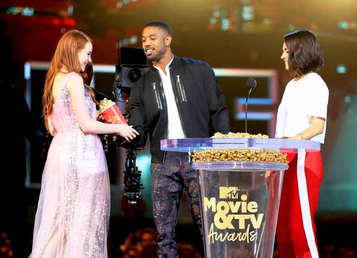 Madelaine Petsch and Mila Kunis present Michael B. Jordan with the Best Villain award for 'Black Panther', onstage during the 2018 MTV Movie And TV Awards at Barker Hangar on June 16, 2018 in Santa Monica, California.