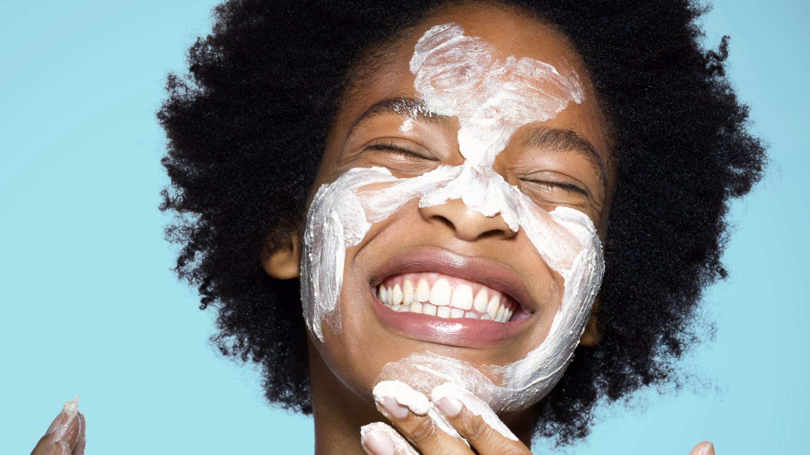 woman washing her face with white lotion skincare black woman with afro