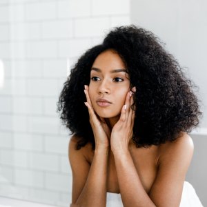 Mixed race woman massaging her face and looking at a mirror