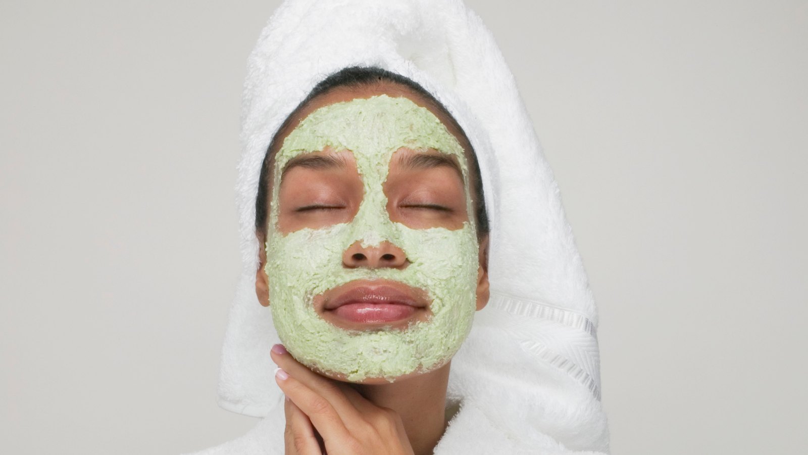 woman wearing a green face mask and white towel spa
