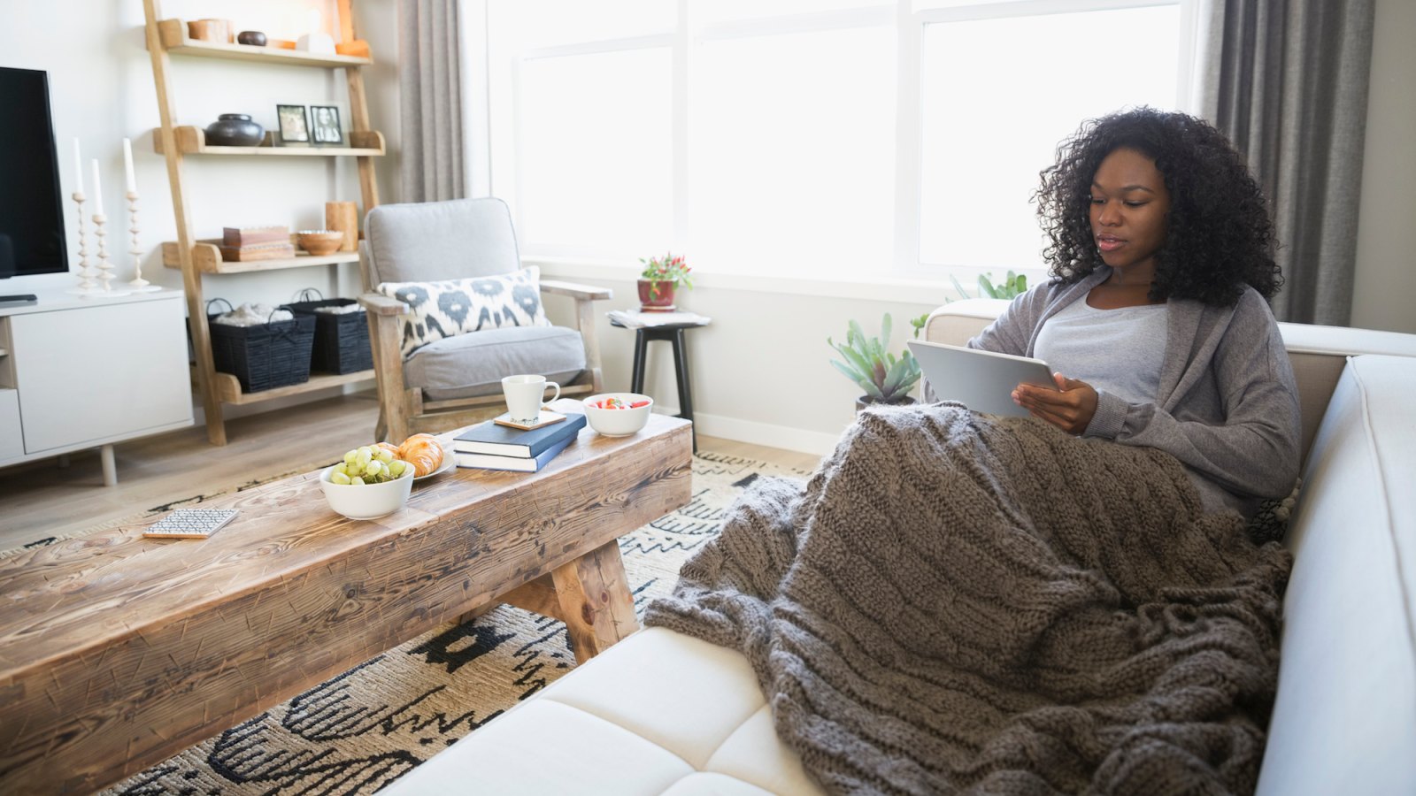 Relaxed woman with blanket using digital tablet on living room sofa