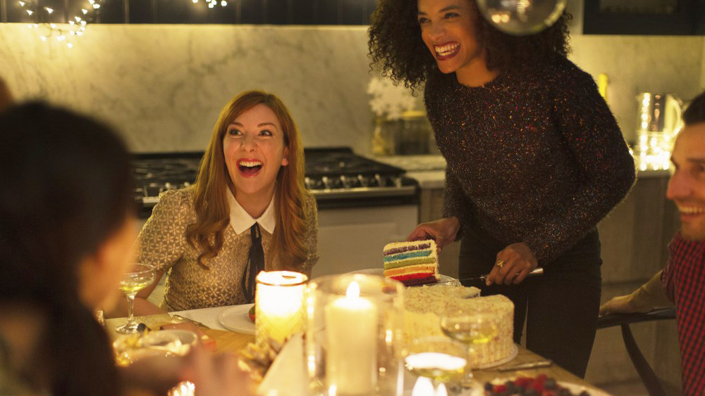 Laughing friends enjoying cake at candlelight Christmas dinner party