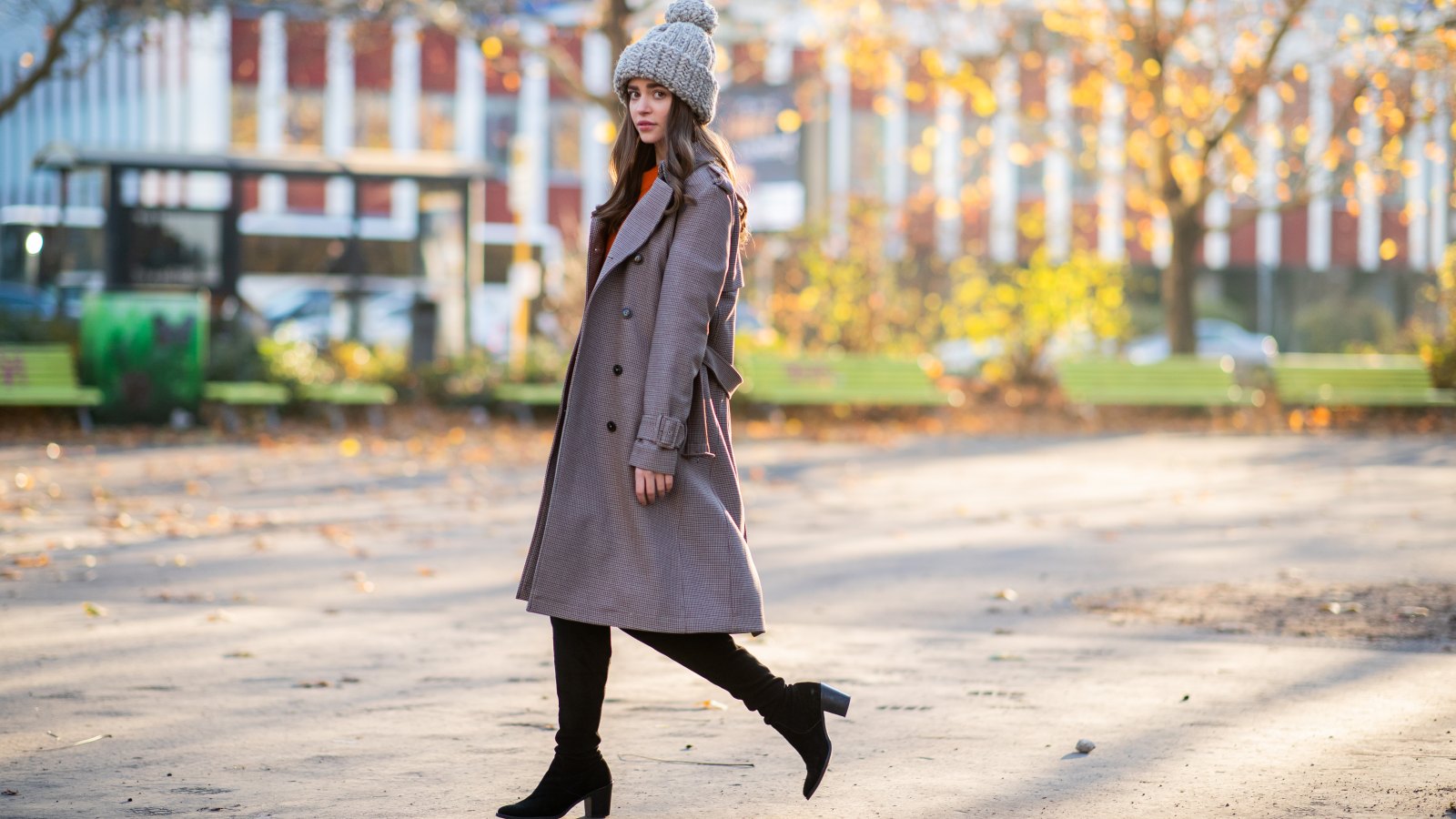 woman wearing boots, a trench coat and knit cap
