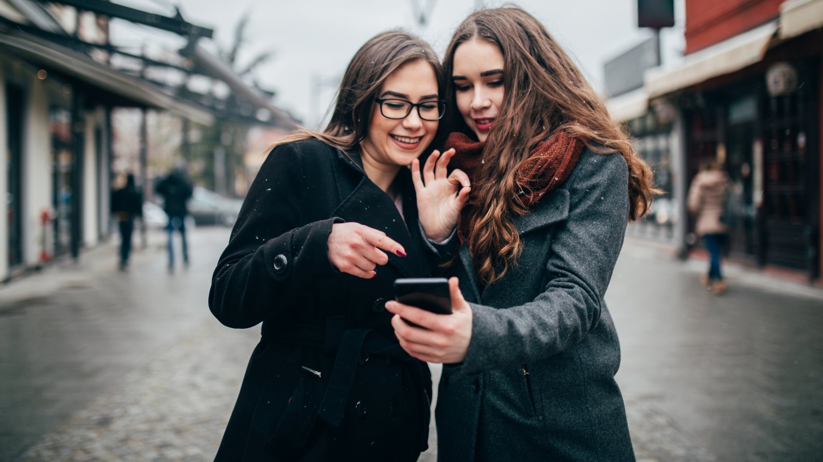 Two female friends using phone downtown