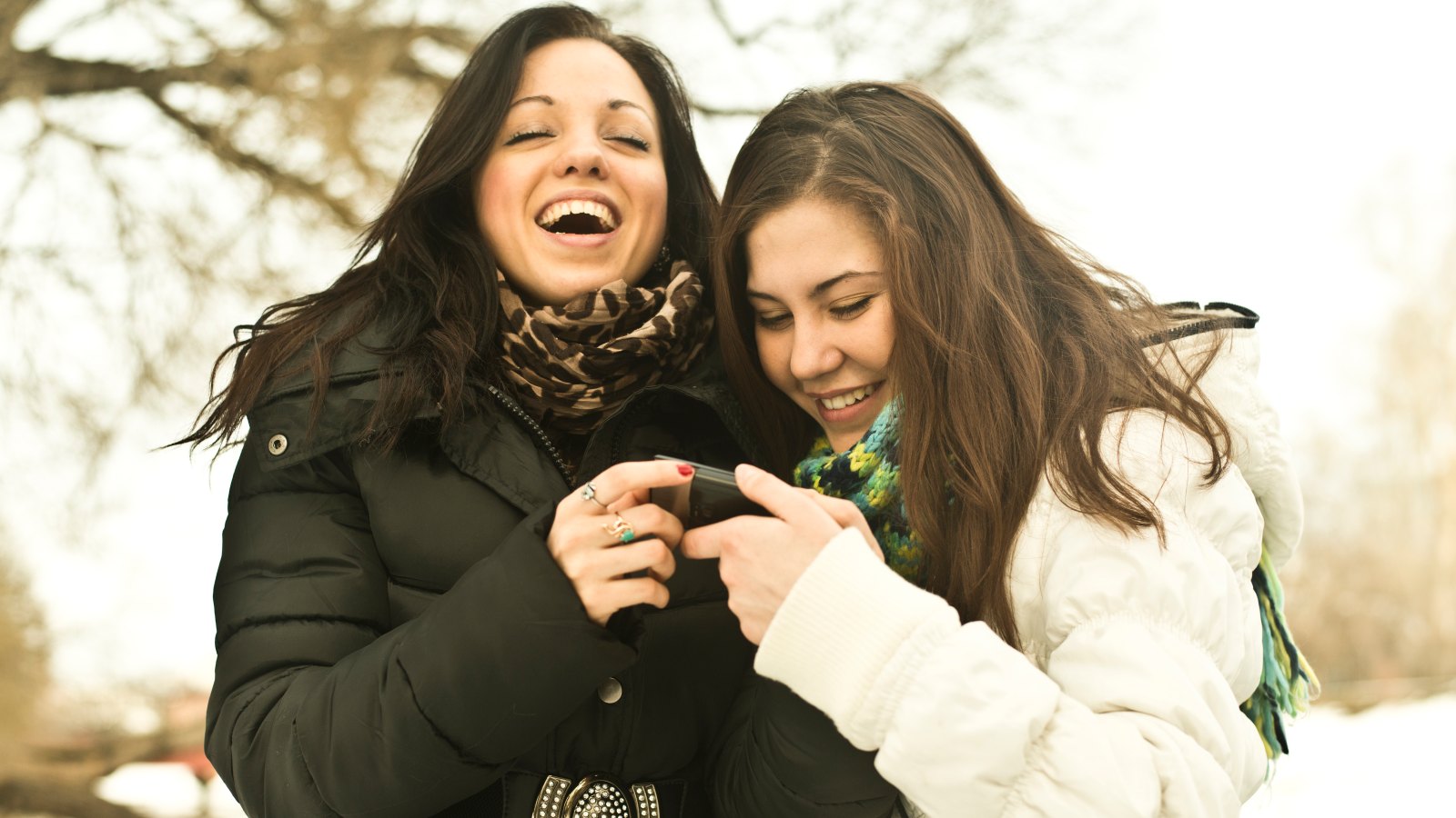 Two young women laughing at mobile phone in park in winter