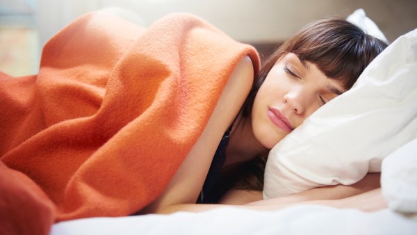 Young woman sleeping underneath an orange blanket and laying her head on a white pillow