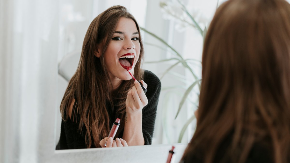 Mirror image of young woman applying lipstick