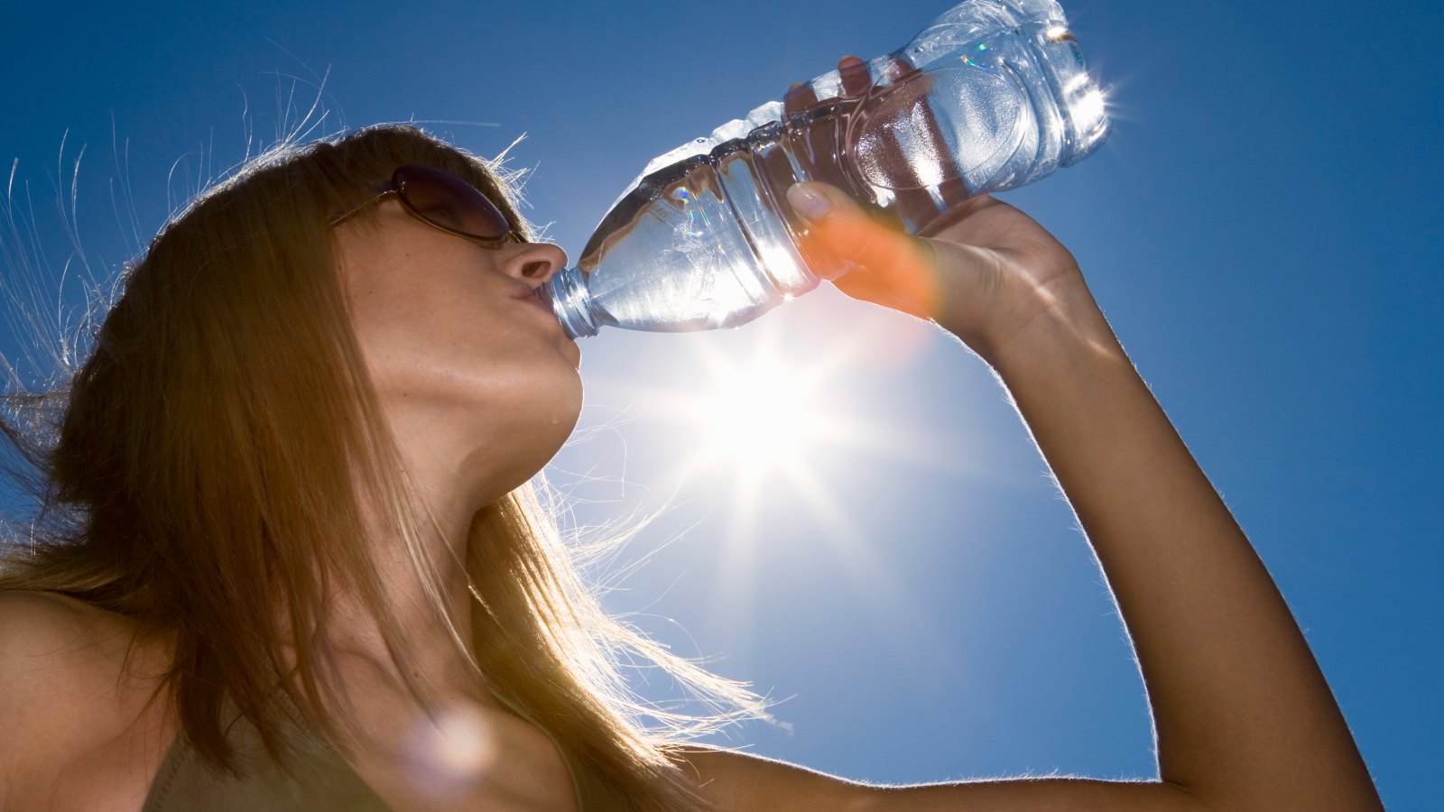 Woman drinking water, low angle view against sky with sun
