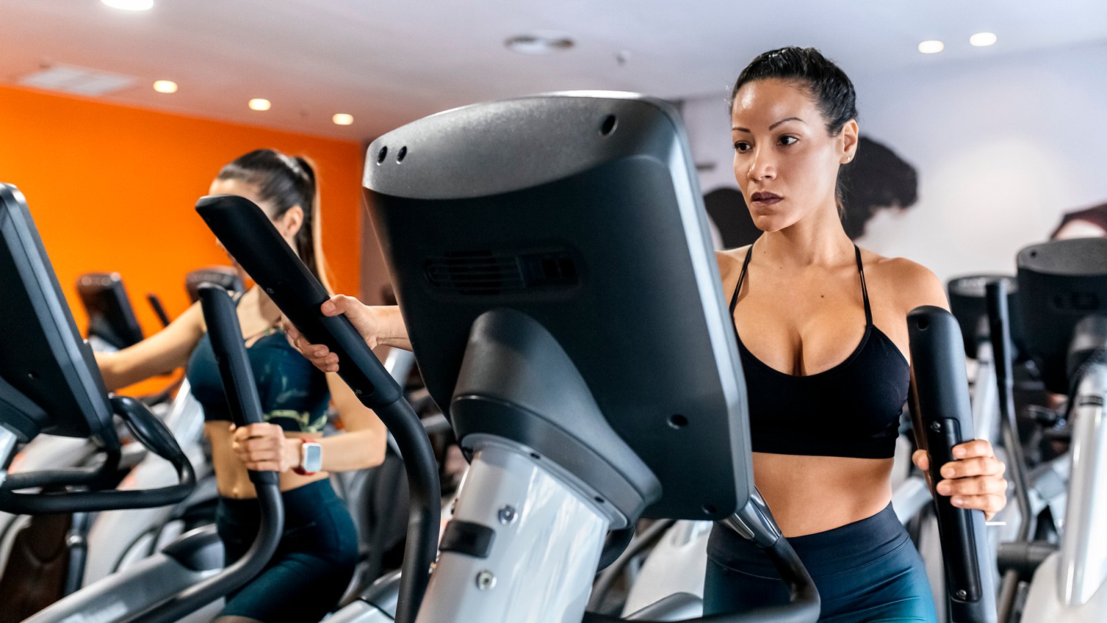 two women working out in gym using a elliptical