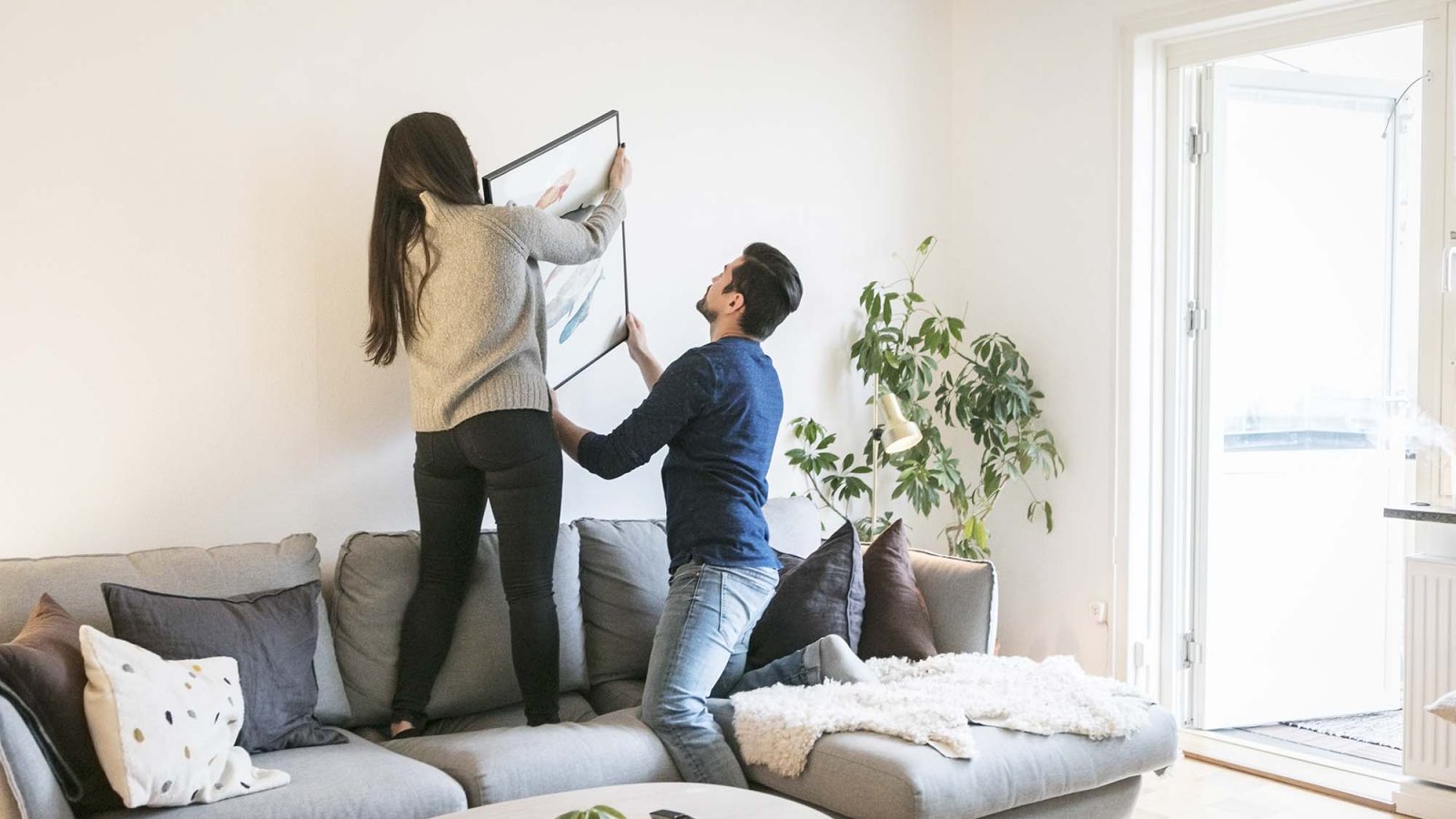 Couple adjusting painting on wall while leaning on sofa at home