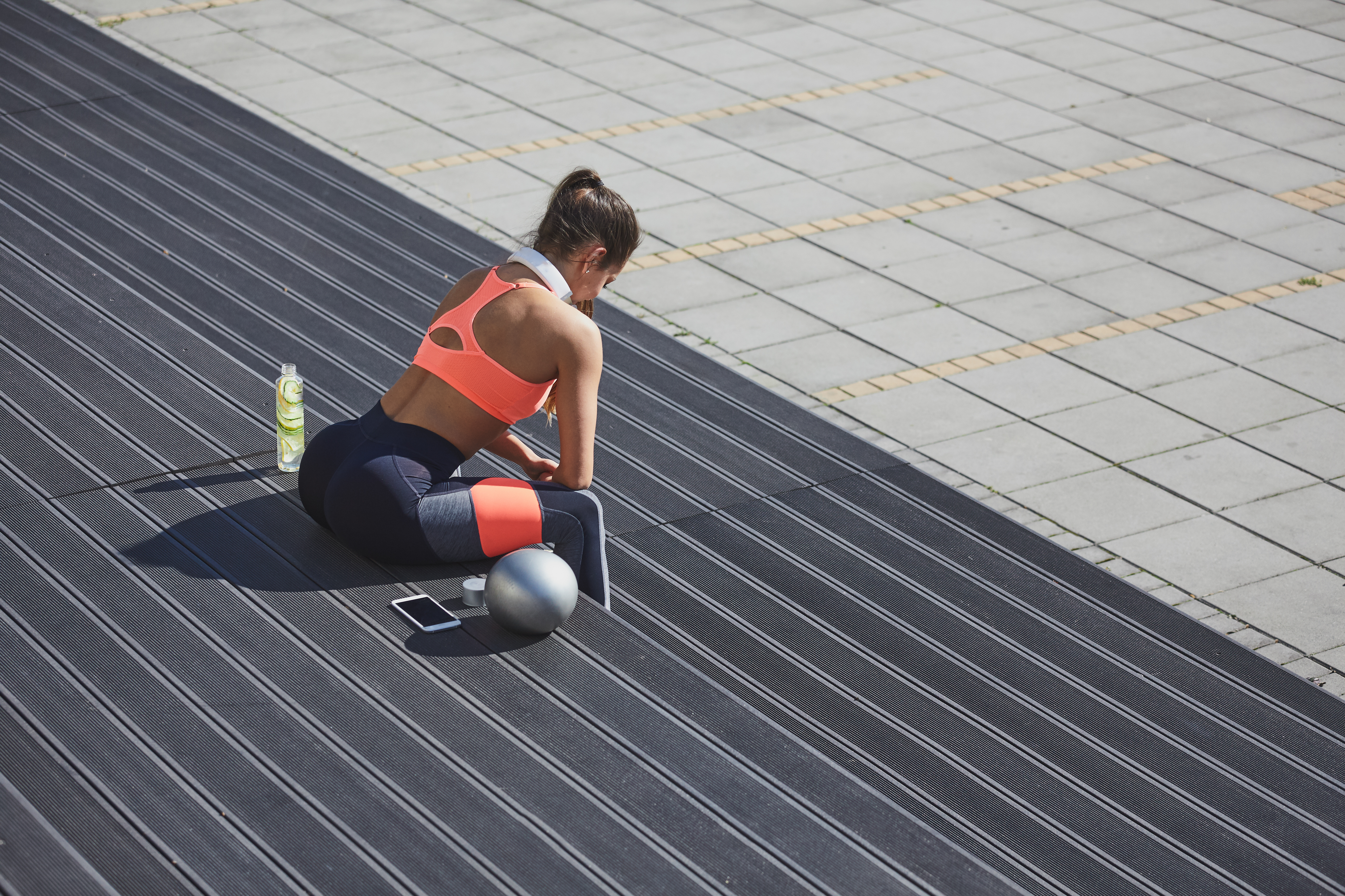 Woman sitting and taking a rest from exercising. Next to her fitness ball, smart phone and refreshing drink.