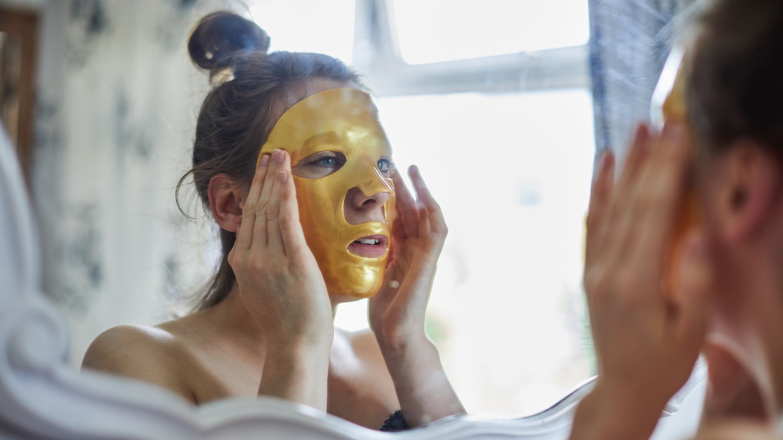 Woman applying a gold face mask in the mirror