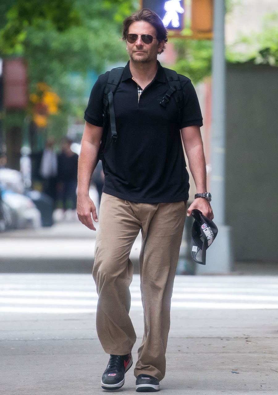 Bradley Cooper Walking in NYC Wearing Khaki Pants Blue Shirt Backpack Sunglasses and Holding A NFL Super Bowl Champions Hat