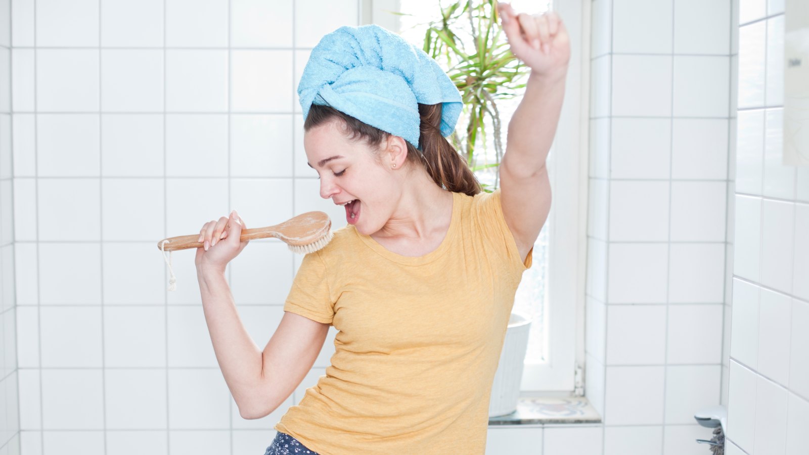 Portrait of young woman singing in the bathroom using massage brush as microphone
