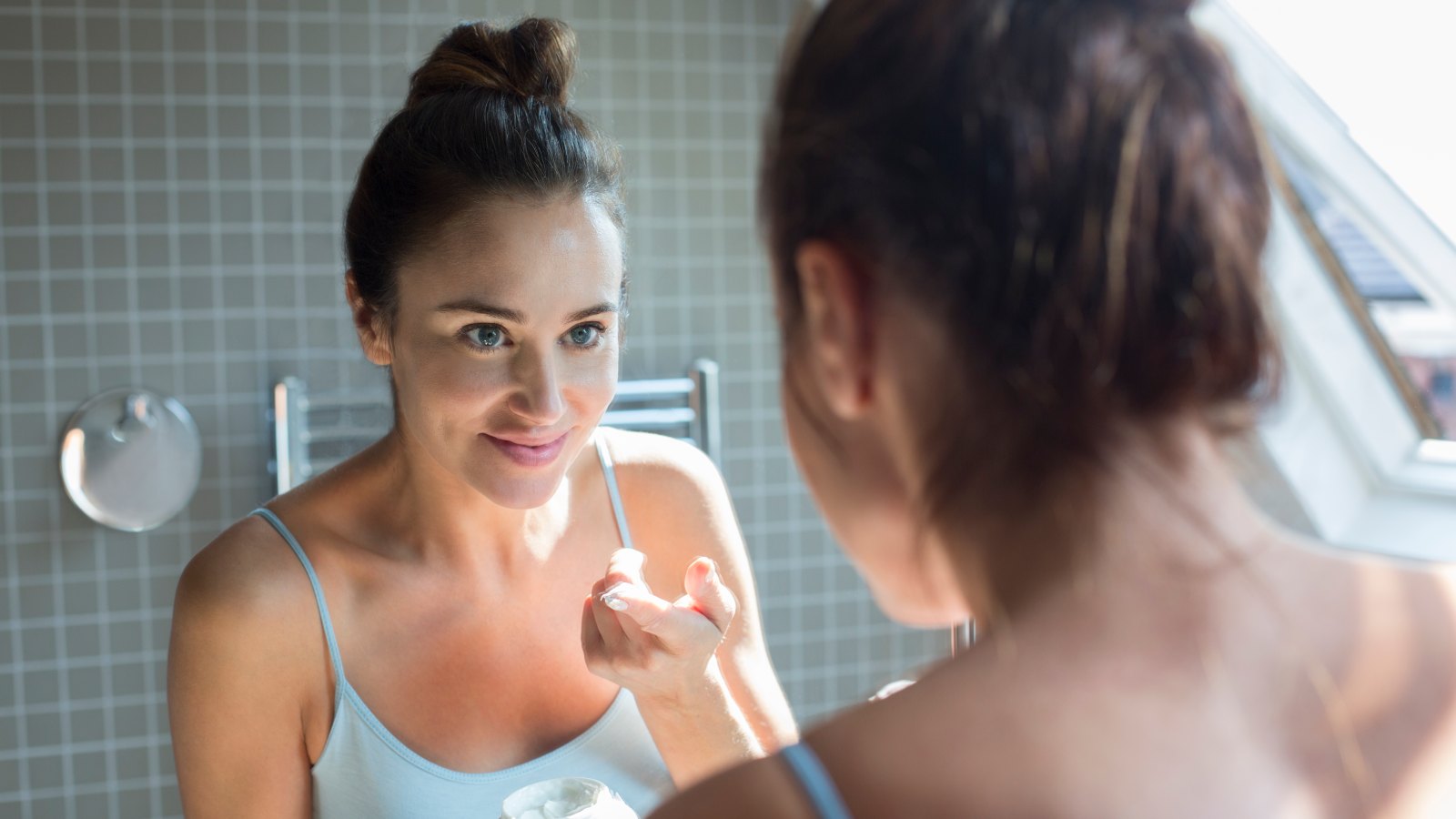 Mid adult woman applying moisturiser in bathroom.