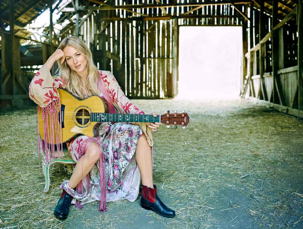 Jewel Holding Guitar in Dress Sitting in a Barn With Hay on the Floor