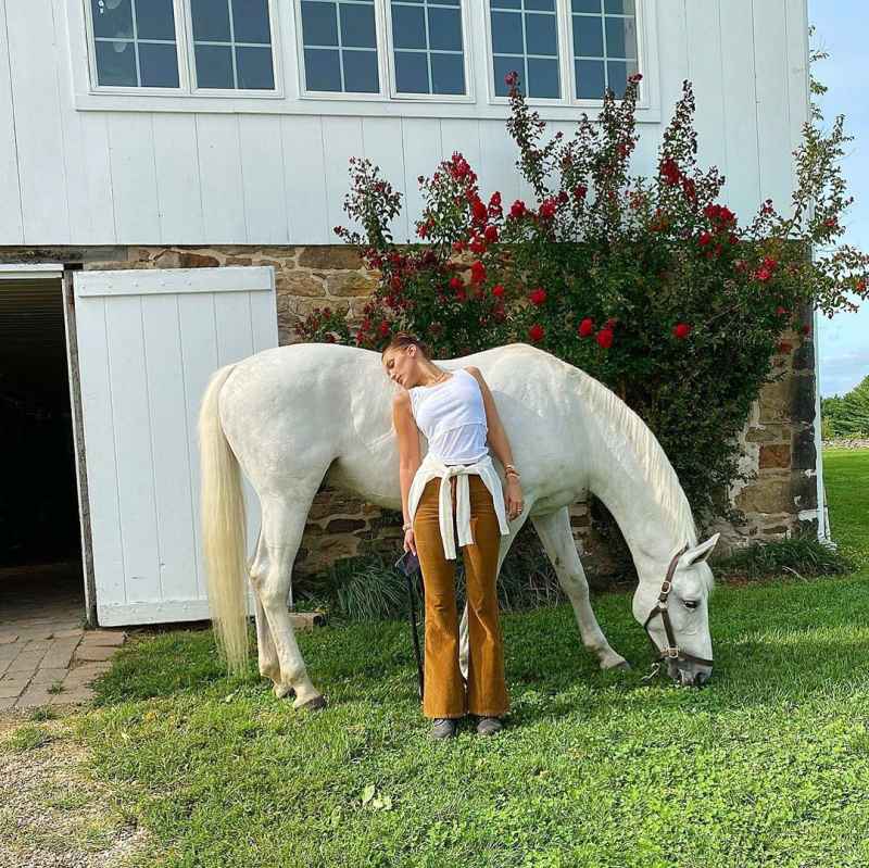 Bella Hadid Posing in Front of Her Horse Wearing flared burnt orange corduroys with a white tank and a cream sweater