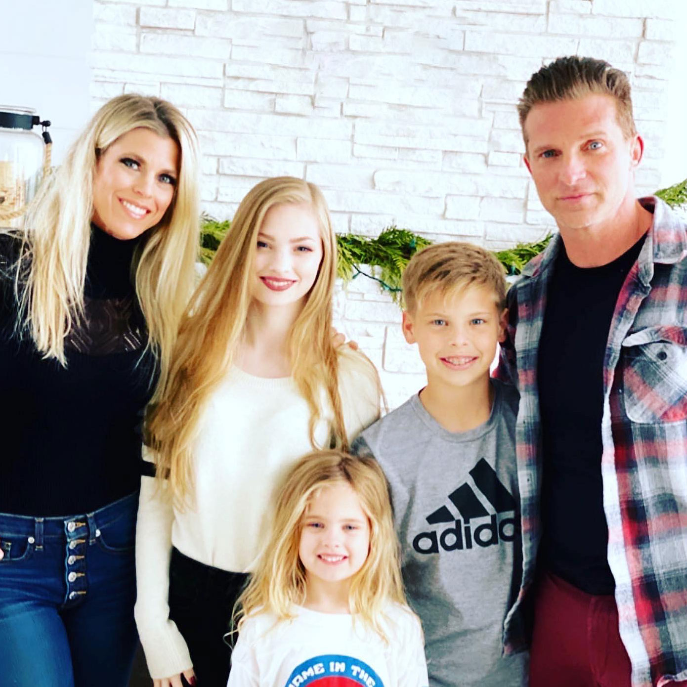 steve burton with wife and three kids posing for photo in front of a white brick wall