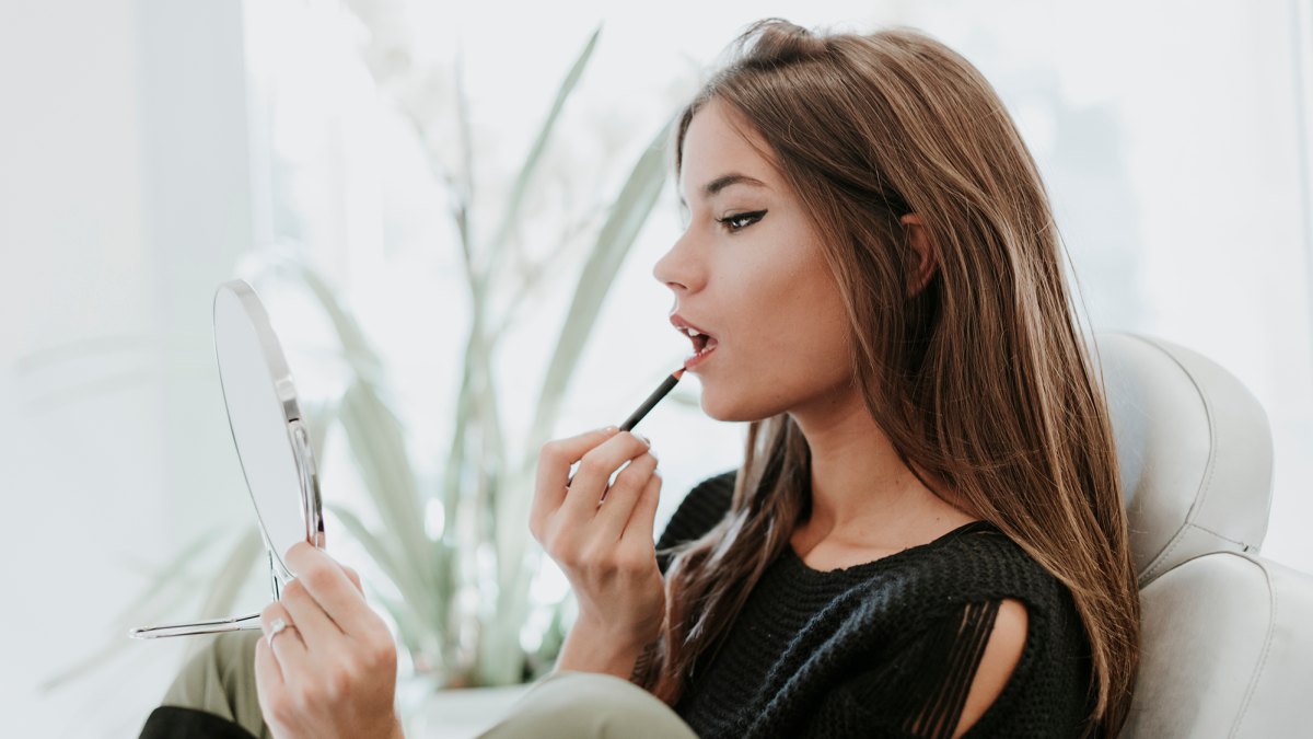 Portrait of young woman using lip pencil
