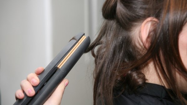 A woman using one of the best flat irons of 2023 to curl her hair.
