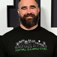 Jason Kelce Smiles Directly at Camera wearing Black T-Shirt that Reads "Football Is A Family Story." in green font