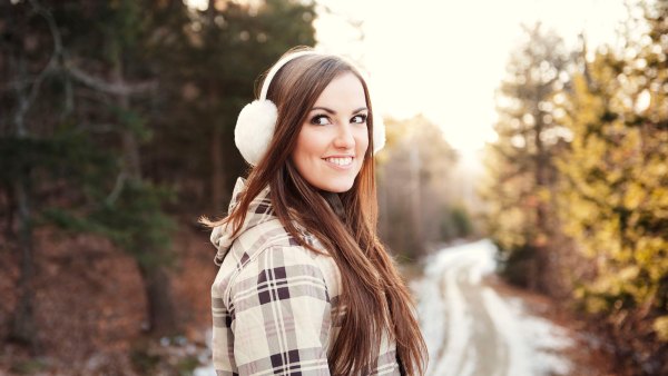 Happy woman wearing ear muff while standing on footpath during winter