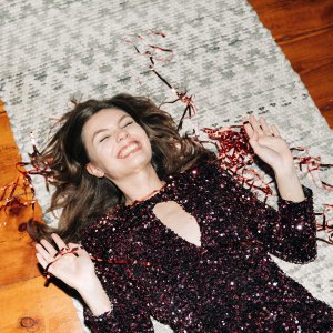 Happy young woman in glittering cocktail dress on carpet floor, flash light, user generated content