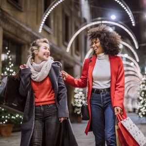 Pretty Young Female Friends Smiling Broadly In Cheerful Manner Having Fun At Shopping Mall, Buying Christmas Gifts