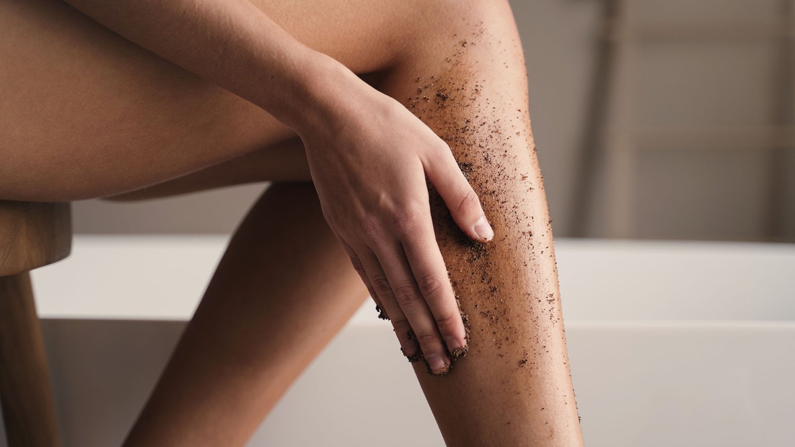 Crop shot of woman hand scrubbing legs with organic scrub in bathroom during anti-cellulite massage. Body and skin care. peeling and exfoliating procedure