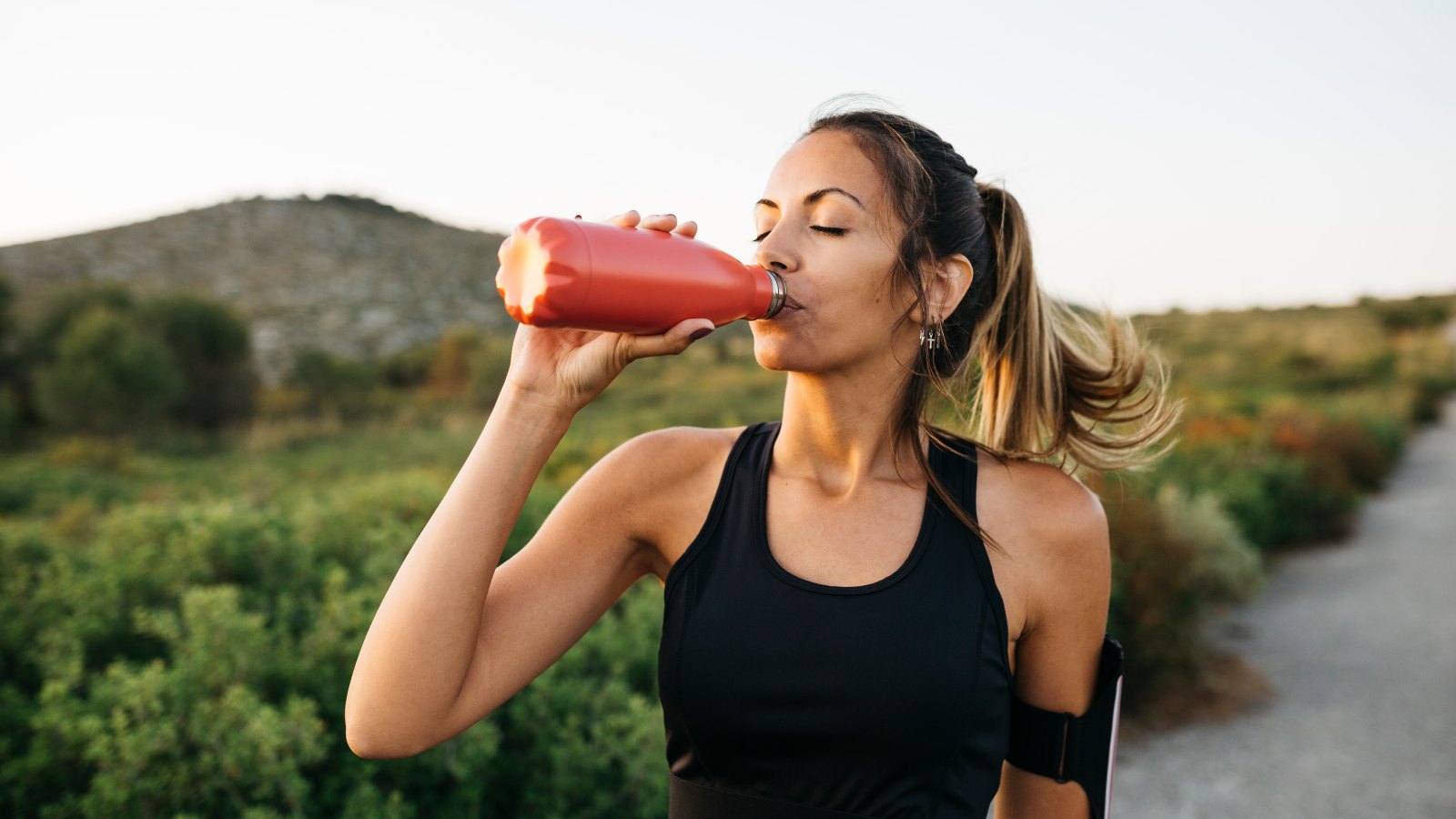 Fit young Woman in black sportswear drinking water from a reusable metal bottle after running workout