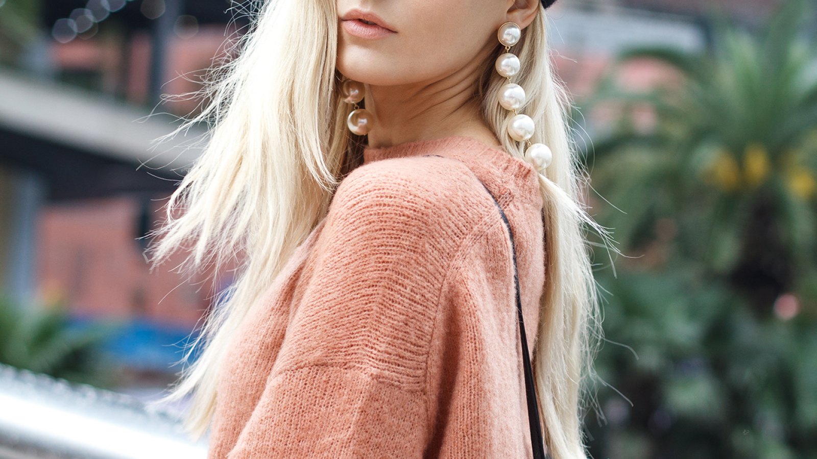 A beautiful young blonde woman dressed in a large warm pink sweater with a black beret and gorgeous earrings.