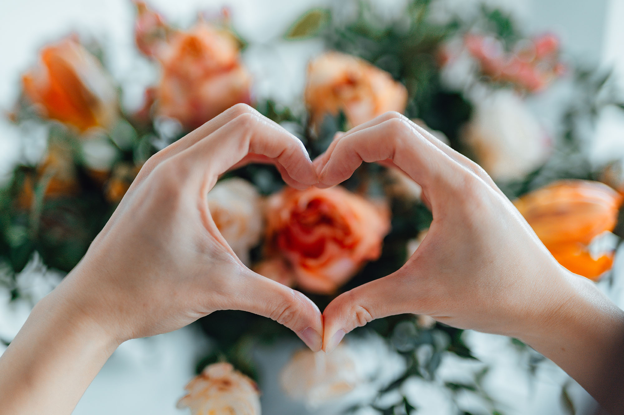 Woman forming a heart with hands against flower bouquet. Heart made with hands. Receiving flower bouquet delivery on Valentine’s day. Online dating concept. Long distance relationship. Dating anniversary.