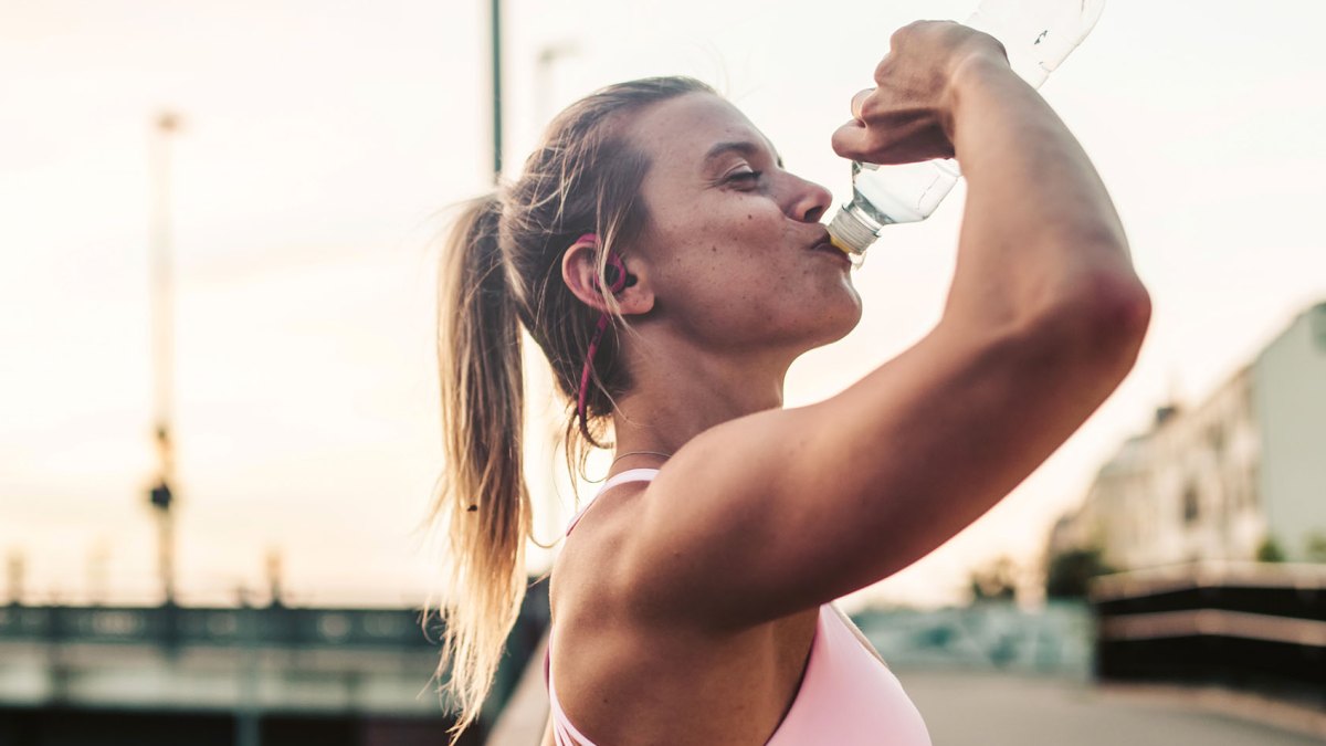Woman after fitness workout,drinking outdoor in the city.