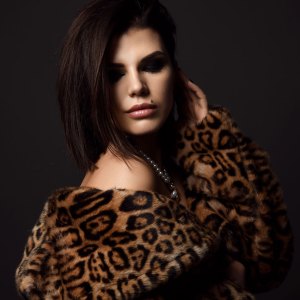 Portrait of young pretty brunette woman model in leopard fur coat with naked shoulders in pearl necklace looking down
