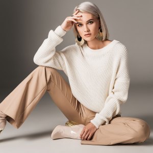 attractive fashionable woman posing in white trendy sweater, beige pants and autumn heels, on grey