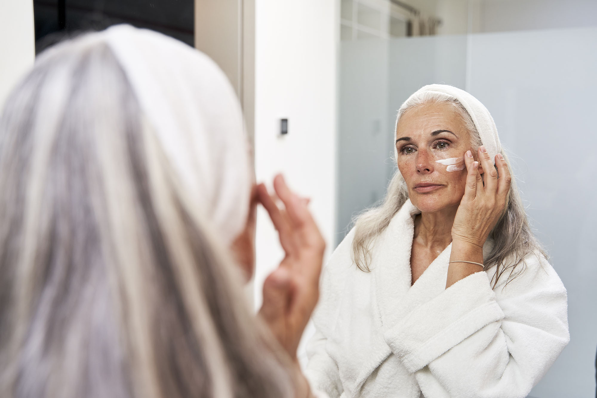 Mature woman applying face cream in bathroom