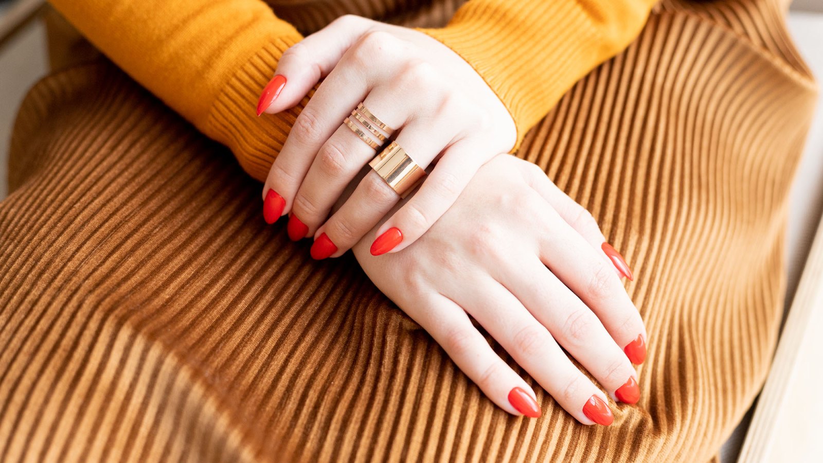 The Young woman's hands with Red manicure and gold rings are on her lap