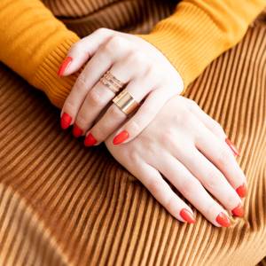 The Young woman's hands with Red manicure and gold rings are on her lap