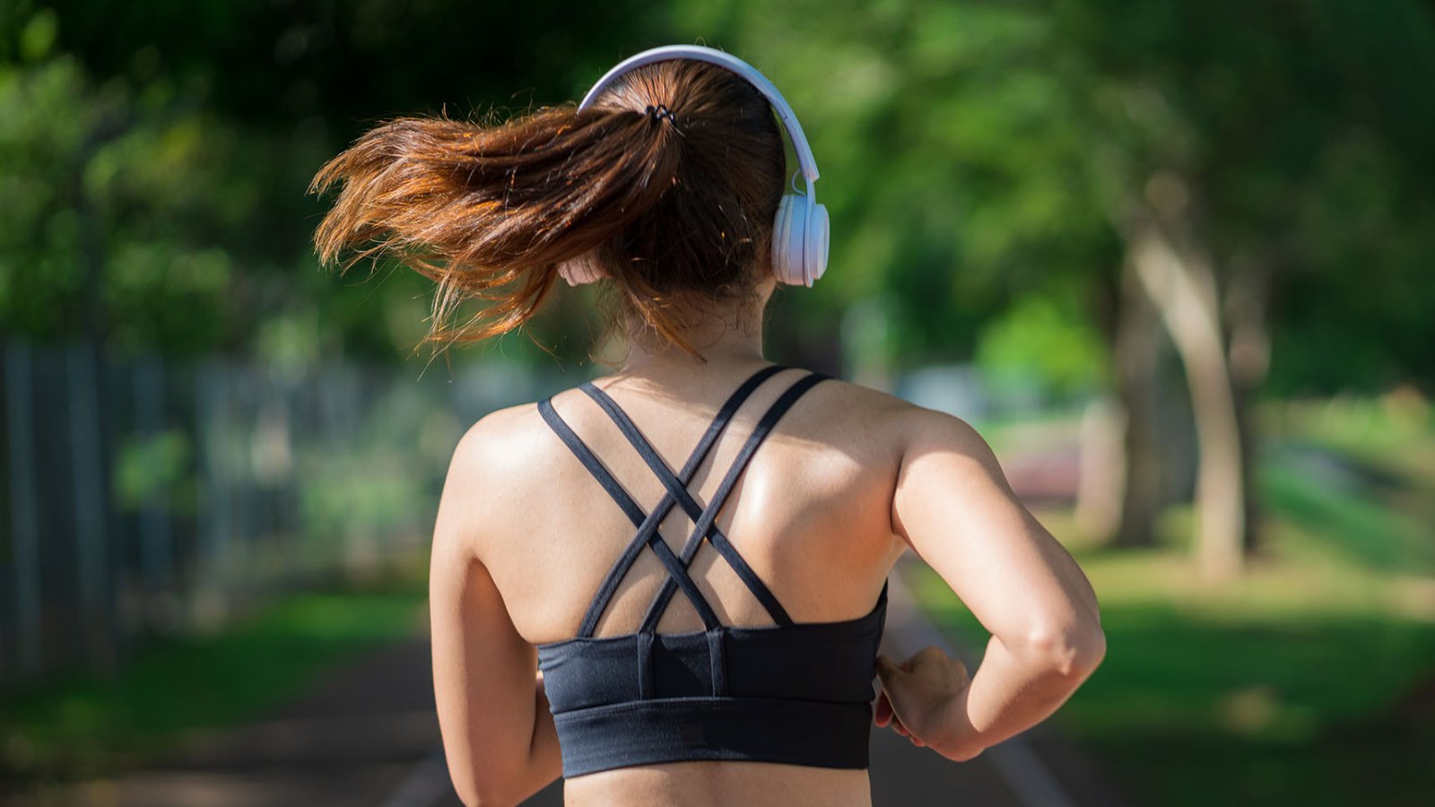 Young fitness sports women runner running in the park. Happy athletic woman listening music on earphones while running in nature in the morning. Healthy fitness woman jogging outdoors.