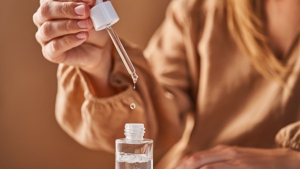 A girl in a beige dress holds a pipette with a drop of serum in her hands. Horizontal.