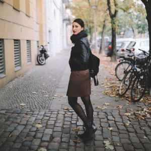 Vintage toned portrait of a young woman in Berlin, wearing a black leather jacket and a beige skirt, walking on the streets of Prenzlauer Berg, near Mitte in the late Autumn day. Street style, casual fashion concept.