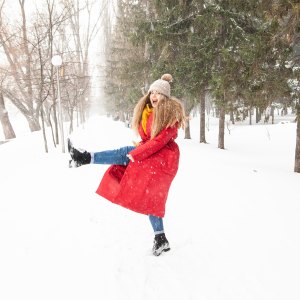 Side view of delighted female in warm clothes jumping and playing with snow in winter garden in city and looking at camera