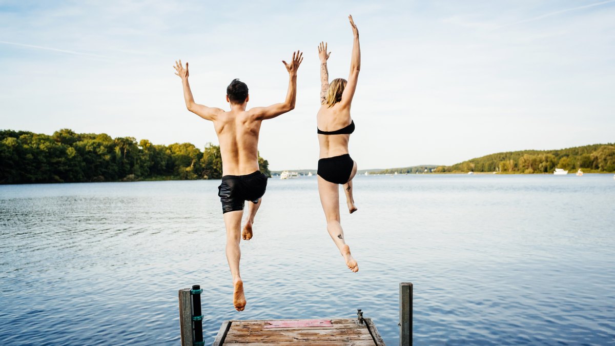 Happy couple jumping into the water from a jetty